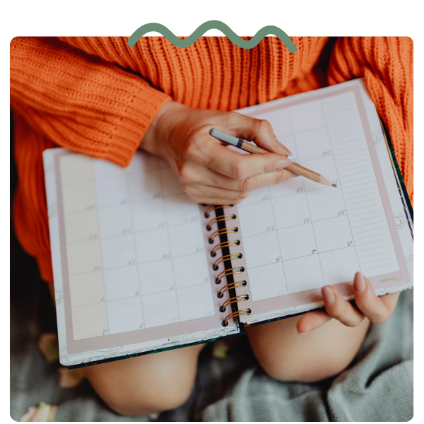woman in sweater writing in calendar planner