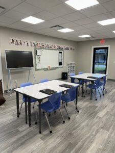 Classroom with tables, chairs, whiteboard, and tv screen